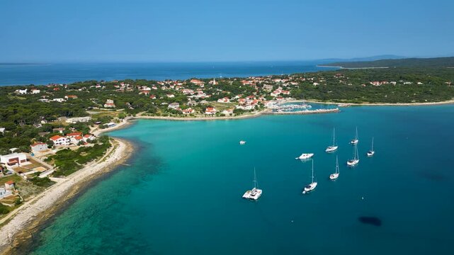Stunning aerial view of Sotorisce Bay on the eastern shore of Silba Island, Croatia, featuring crystal clear turquoise water, a sandy seabed, and a protected harbor filled with white sailboat