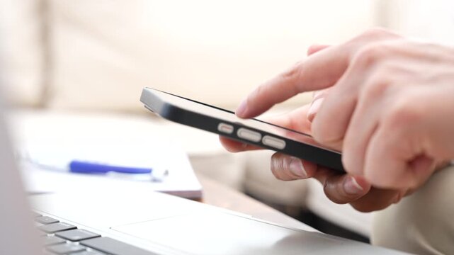 Professional using smartphone beside laptop for CRM communication, customer support and email workflow. Mobile productivity, business software, digital communication and remote work concept.