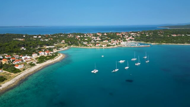 Stunning aerial view of Sotorisce Bay on the eastern shore of Silba Island, Croatia, featuring crystal clear turquoise water, a sandy seabed, and a protected harbor filled with white sailboat