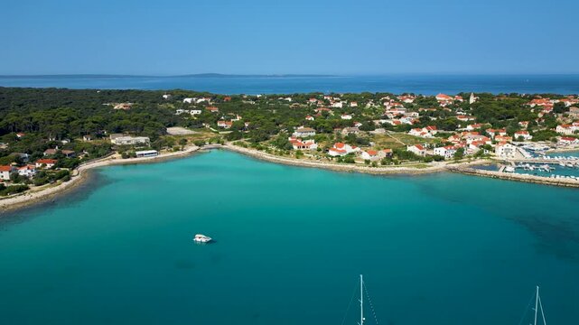 Stunning aerial view of Sotorisce Bay on the eastern shore of Silba Island, Croatia, featuring crystal clear turquoise water, a sandy seabed, and a protected harbor filled with white sailboat