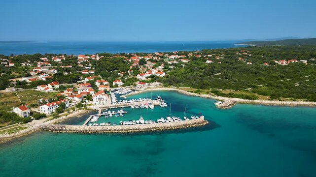 Stunning aerial view of Sotorisce Bay on the eastern shore of Silba Island, Croatia, featuring crystal clear turquoise water, a sandy seabed, and a protected harbor filled with white sailboat