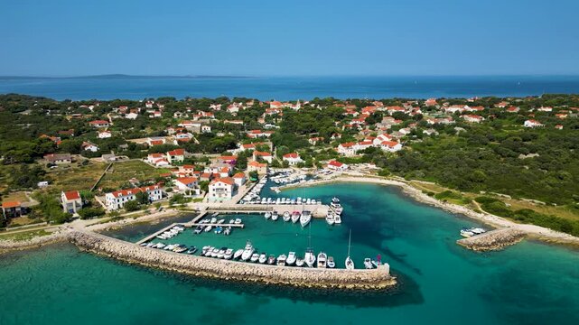 Stunning aerial view of Sotorisce Bay on the eastern shore of Silba Island, Croatia, featuring crystal clear turquoise water, a sandy seabed, and a protected harbor filled with white sailboat