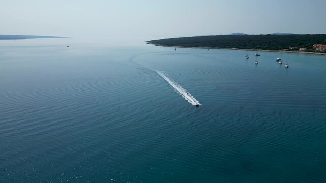 An exhilarating aerial drone shot over Silba Island, Croatia, capturing a water skier carving through the crystal-clear, turquoise sea behind a speeding motorboat. The top-down view beautifully frames