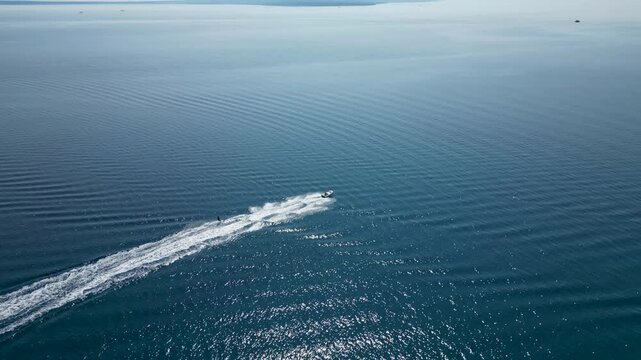 An exhilarating aerial drone shot over Silba Island, Croatia, capturing a water skier carving through the crystal-clear, turquoise sea behind a speeding motorboat. The top-down view beautifully frames