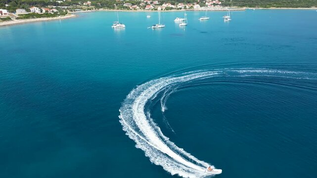 An exhilarating aerial drone shot over Silba Island, Croatia, capturing a water skier carving through the crystal-clear, turquoise sea behind a speeding motorboat. The top-down view beautifully frames