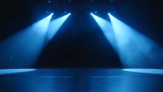 Four bright blue stage spotlights shining down from a dark rigging onto a polished empty floor, creating a luminous focal point with visible volumetric light beams and haze in a theater.