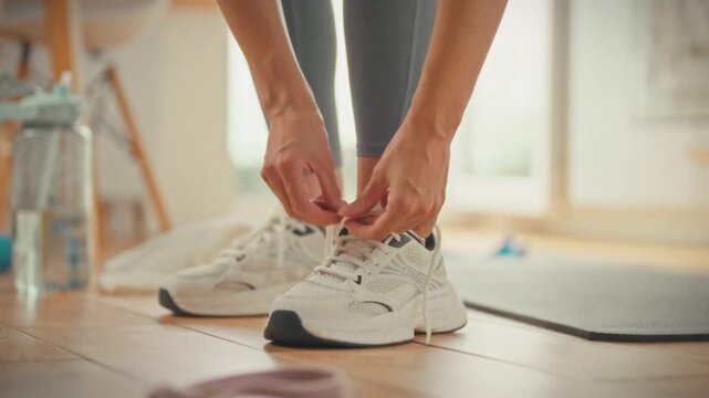 A girl ties her sneakers in the kitchen getting ready for training at home. The concept of comfortable exercise at home without prying eyes and pressure