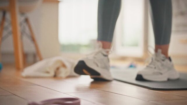 A sportswoman in leggings reaches for a bottle of water against the backdrop of a yoga mat. The concept of hydration as an important part of an effective home workout
