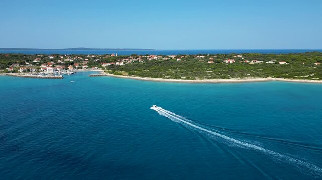 Aerial drone view of a speedboat approaching Silba Island in Croatia across the deep blue Adriatic Sea. Scenic Mediterranean coastline, turquoise waters and a charming island village create an idyllic