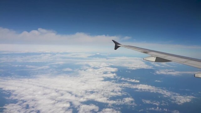 View from airplane window showing wing over clouds and blue sky.