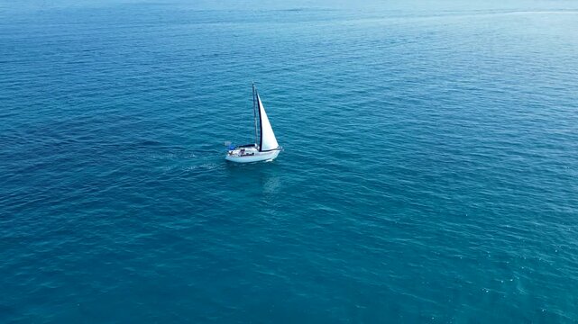 A stunning aerial drone perspective showcasing a white sailboat gliding through the crystal-clear, turquoise waters of Silba Island, Croatia. The shot beautifully captures the contrast between the