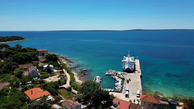 A breathtaking aerial drone panorama of Zalic port on Silba Island, Croatia. The shot showcases the vibrant turquoise harbor, a docked ferry, and the charming coastal village stretching across the