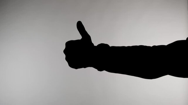 An anonymous silhouette of a man standing against a white background and holding his hand up in a thumbs up gesture, then turning it down in a sign of disapproval