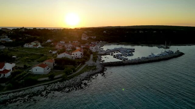 A stunning aerial drone shot capturing the warm golden sunset over the Sotorisce bay and Mulj harbor area on Silba Island, Croatia. The perspective showcases the sheltered marina filled with boats