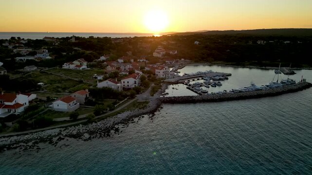 A stunning aerial drone shot capturing the warm golden sunset over the Sotorisce bay and Mulj harbor area on Silba Island, Croatia. The perspective showcases the sheltered marina filled with boats