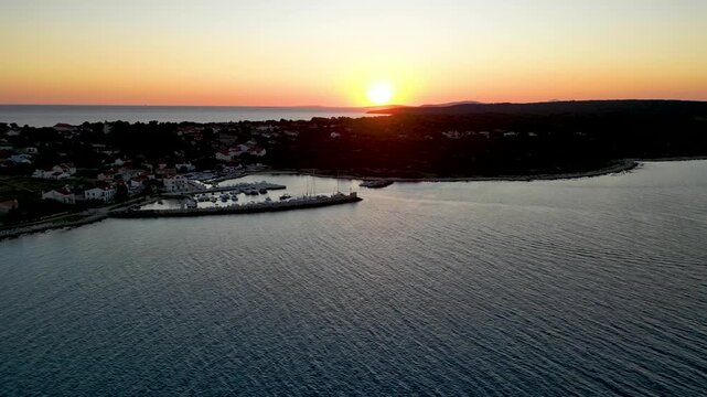 A stunning aerial drone shot capturing the warm golden sunset over the Sotorisce bay and Mulj harbor area on Silba Island, Croatia. The perspective showcases the sheltered marina filled with boats