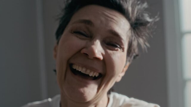 Closeup portrait of mid aged Caucasian woman looking into camera, transitioning from hysterical laughing to crying. Clip is suitable for mental health awareness campaigns or psychiatric clinic promos