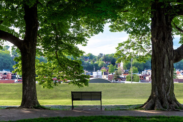 Obraz premium Park bench framed by mature shade trees overlooking historic downtown Galena, Illinois, on a summer morning