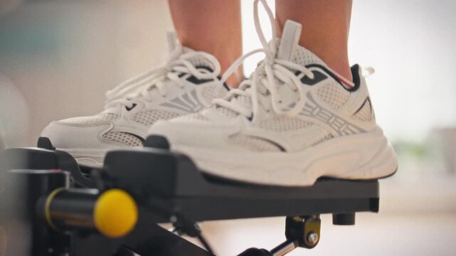 Stepping onto stepper in bright home gym, female athlete in leggings performs cardio exercise. This affordable routine boosts fitness, showcasing convenient at-home training that energizes daily life