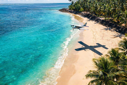 Small propeller plane flying over a tropical beach with clear blue water and palm trees