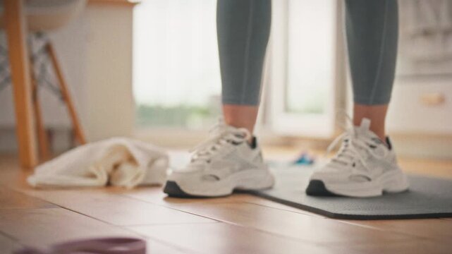 A girl in a sports uniform takes a bottle of water against the background of a laid out rug at home. The concept of a healthy lifestyle and conscious care of the body through regular exercise
