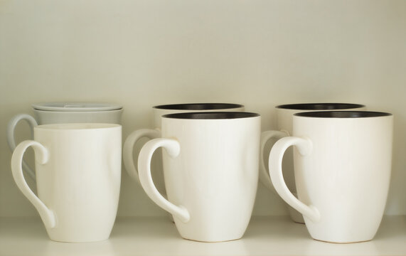 White ceramic mugs neatly arranged on a kitchen cupboard shelf, showing everyday household kitchenware.