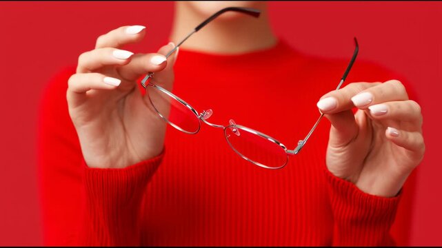 Woman holds red glasses in front of red background while wearing a red shirt