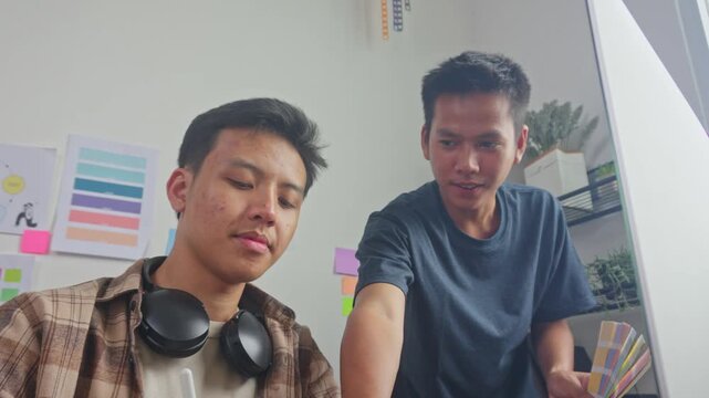 Graphic designers collaborating to match color palette swatches with digital layout on screen