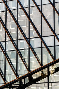 Strong diagonal beams cut across a glass building facade, where windows, reflection and urban architecture reveal the structure as a layered geometric surface