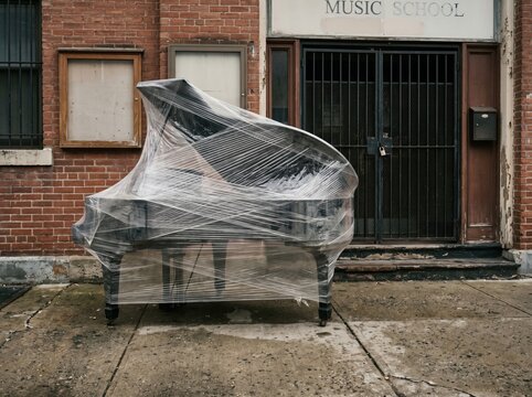 Shrink wrapped grand piano outside music school doorway for arts cuts concept