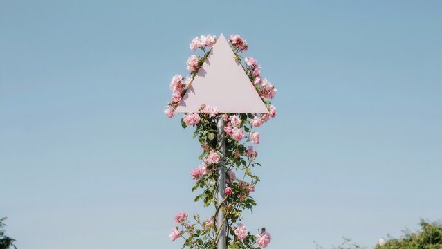 Pink triangle sign covered in roses against a clear blue sky
