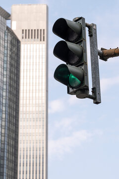 Green traffic light hangs beside a tall building facade, where signal equipment, urban street details and sky frame vertical city architecture