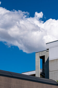 White cloud floats above a building corner against blue sky, where facade lines, rooftop edge and urban architecture create a crisp exterior view