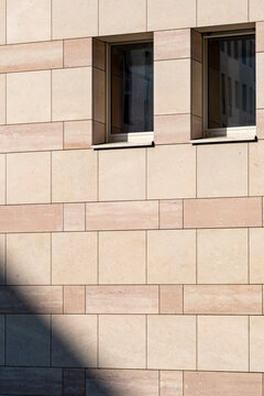 Small stone facade windows catch hard sunlight and shadow, where beige wall blocks, urban architecture and pattern create exterior detail