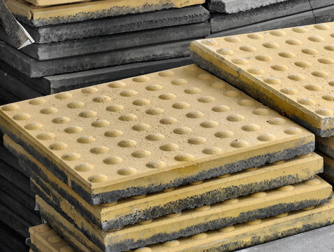 A stack of yellow tactile paving blocks or braille bricks on a construction site. Designed to guide visually impaired people, representing universal design and urban accessibility.