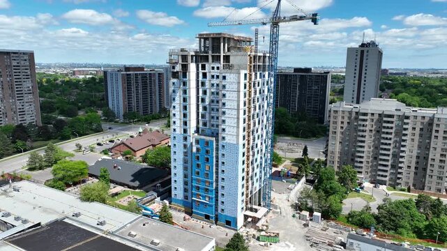 Aerial view of a high-rise public housing residential tower under construction, surrounded by established apartment buildings in a dense urban community.