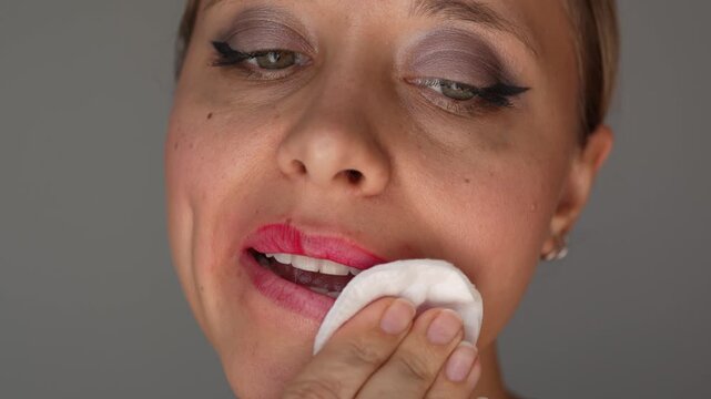 Young woman removing red lipstick with a cotton pad. Lip makeup removal, cleansing and skincare routine concept
