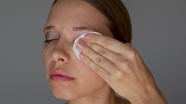 Close-up of young woman removing eye makeup with a cotton pad. Daily cleansing routine, gentle skincare and cosmetic remover concept