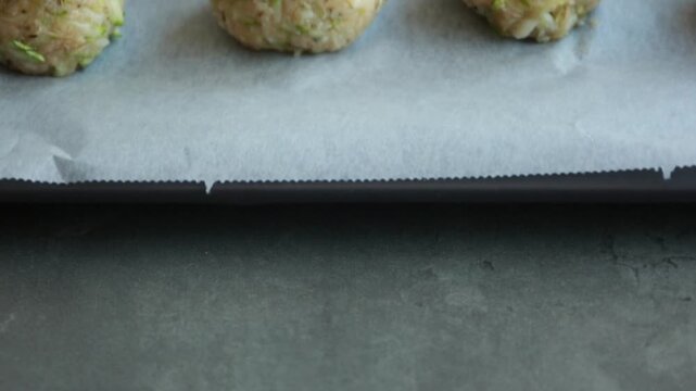 Close-up of raw, unbaked zucchini balls tots arranged in neat rows on a baking sheet lined with parchment paper