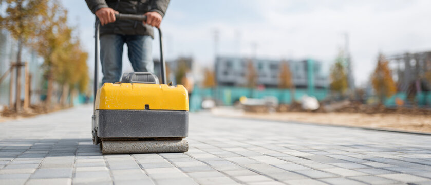 Worker operating compactor on paved walkway