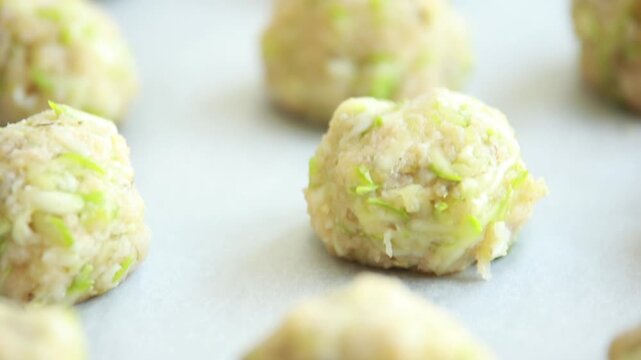 Close-up of raw, unbaked zucchini balls tots arranged in neat rows on a baking sheet lined with parchment paper