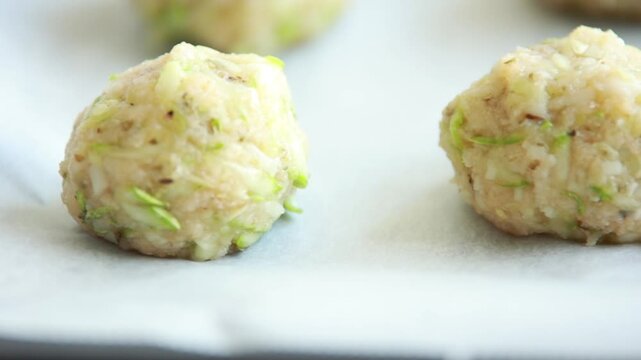 Close-up of raw, unbaked zucchini balls tots arranged in neat rows on a baking sheet lined with parchment paper