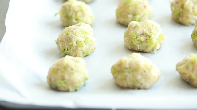 Close-up of raw, unbaked zucchini balls tots arranged in neat rows on a baking sheet lined with parchment paper