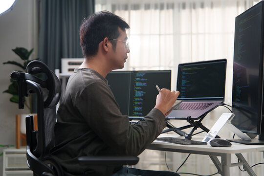Focused Programmer Writing Code on Laptop and Desktop Monitors in Office Setup