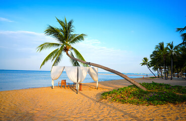 Naklejka premium Beach setting with tent and palm trees. Beneath palm tree, secluded beach cabana with white curtains and chairs offers relaxation for guests. Picturesque Long Beach on ​​Phu Quoc Island in Vietnam