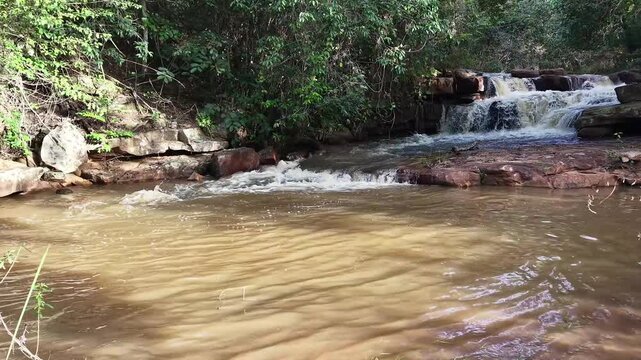 V&iacute;deo de queda d'&aacute;gua natural correndo sobre pedras escuras cercada por vegeta&ccedil;&atilde;o densa de floresta tropical no Parque Nacional da Chapada Diamantina, Bahia, Brasil.