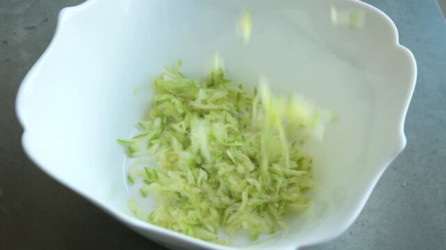 Close-up of freshly grated zucchini inside a white mesh nut milk bag or cheesecloth, ready to be squeezed and drained of excess water