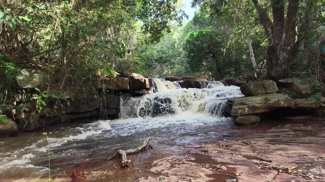 V&iacute;deo de queda d'&aacute;gua natural correndo sobre pedras escuras cercada por vegeta&ccedil;&atilde;o densa de floresta tropical no Parque Nacional da Chapada Diamantina, Bahia, Brasil.