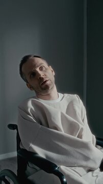 Vertical dolly in portrait of middle aged Caucasian man in straightjacket sitting in wheelchair, staring blankly into camera. Footage is ideal for psychiatric clinic promotions, vertical