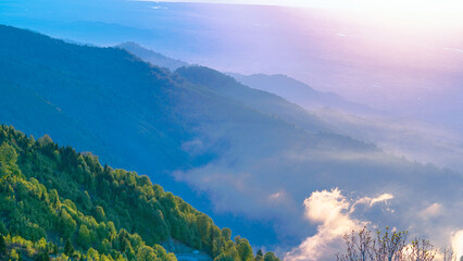 Fototapeta premium Misty mountain ridges covered in lush green forests during a golden sunrise